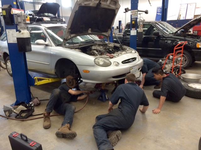 three students working under a car