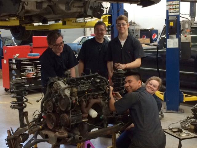 five students working on a car engine